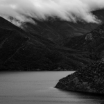 Black and white photo of lake surrounded by mountains with low cloud cover.