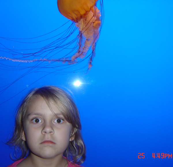 Photo of associate editor Hannah Janson as a child standing in front of a jellyfish in an aquarium tank.