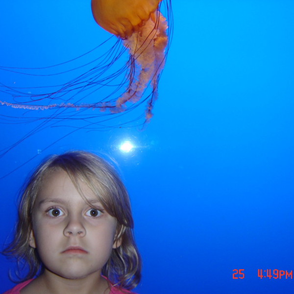 Photo of associate editor Hannah Janson as a child standing in front of a jellyfish in an aquarium tank.