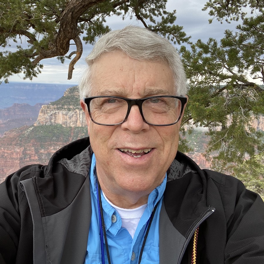 Headshot of Michael Roberts against the Grand Canyon in a blue shirt and grey jacket.
