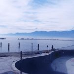 Photograph of an empty pool by the water, a cloudy sky above.