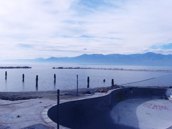 Photograph of an empty pool by the water, a cloudy sky above.