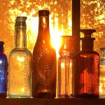 A row of empty glass bottles on a window sill backlit by a sunset